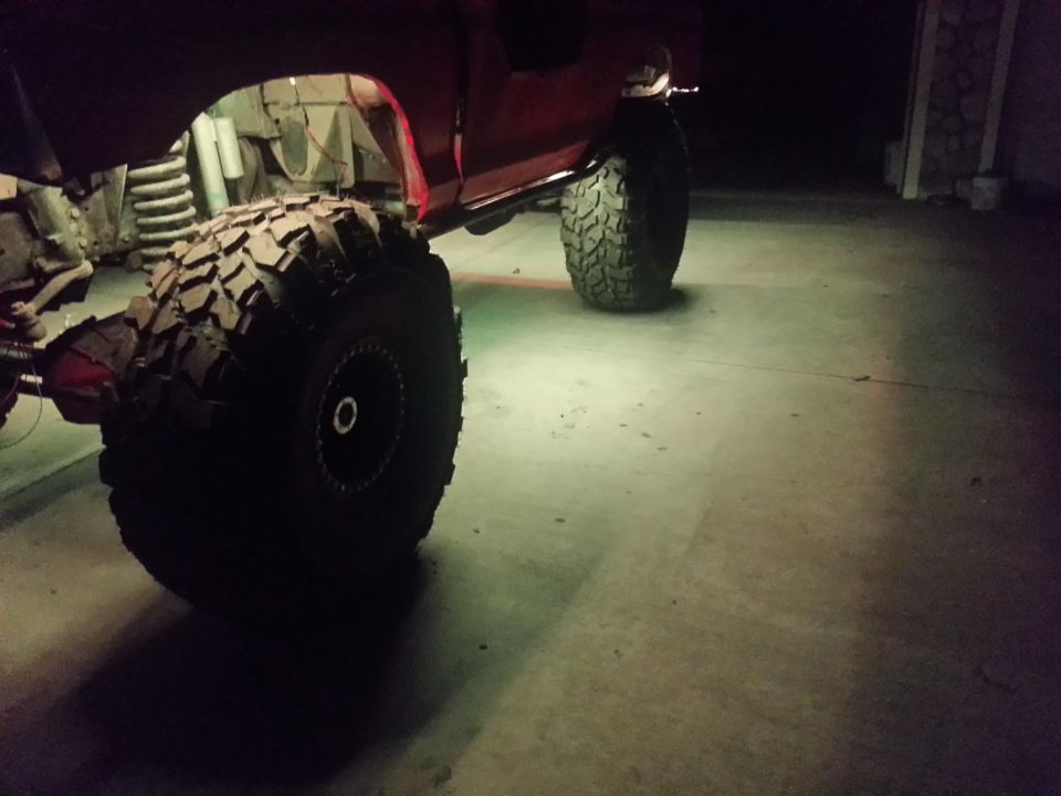 Modified off-road vehicle with large tires and visible suspension components, illuminated by underglow lights