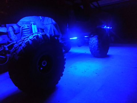 1978 Ford Bronco - A vehicle chassis with large tires is illuminated by blue underglow lights.
