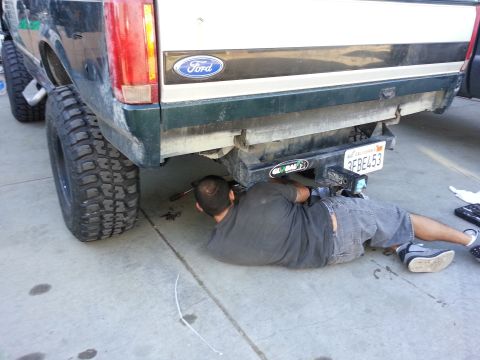 1978 Ford Bronco - Mechanic works on the rear end of a lifted Ford truck, possibly a F-Series model from the early 1990s.