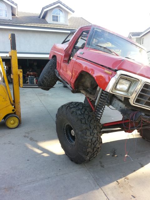 1978 Ford Bronco - A red off-road vehicle is being lifted by a forklift, showing its suspension and exposed wiring.