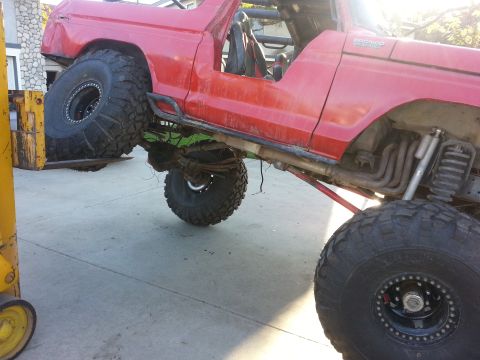 1978 Ford Bronco - A heavily modified red 1978 Ford Bronco is shown with its suspension and exhaust system visible, being supported by a forklift.