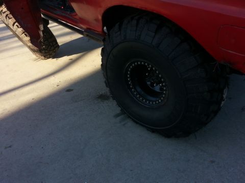 1978 Ford Bronco - Close-up of the passenger-side rear tire on a red 4x4: an aggressive mud-terrain tire mounted on a black bolt-on beadlock wheel, filling th…