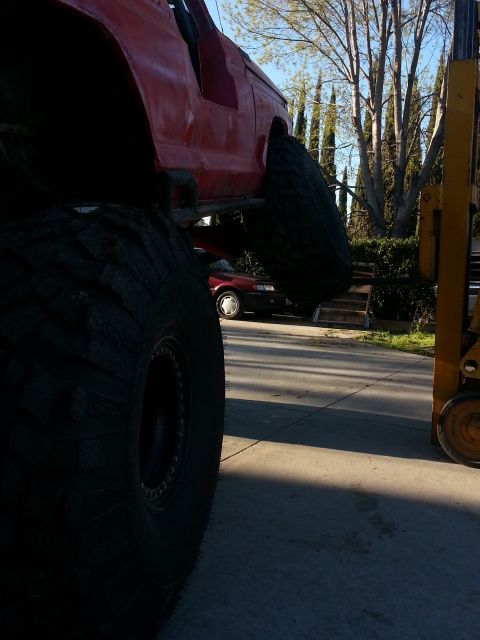 1978 Ford Bronco - A red off-road vehicle is partially visible next to a forklift, with another car in the background.