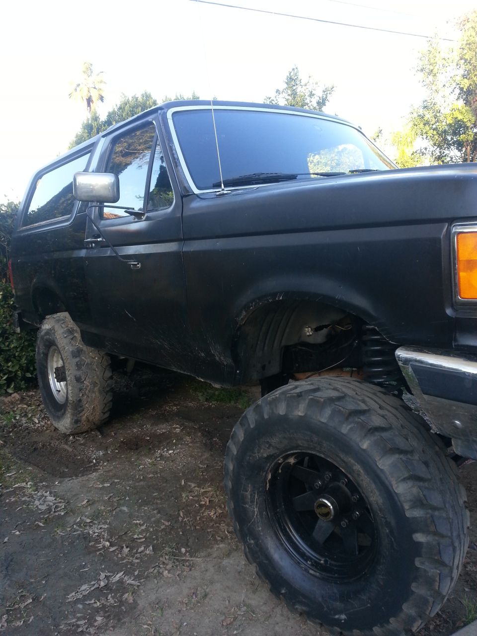 Flat black lifted full-size Bronco on dirt with front fender opened and mud tires