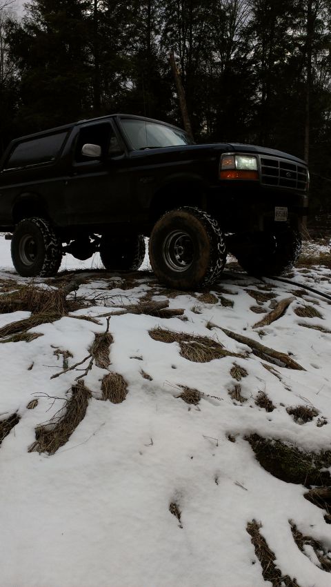 1995 Ford Bronco - Black 1995 Ford Bronco sits on a snow-covered incline with trees in the background.