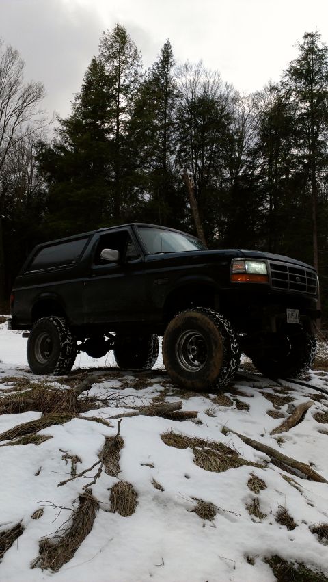 1995 Ford Bronco - A lifted black SUV sits on a snowy, wooded path, its tires ready for adventure.