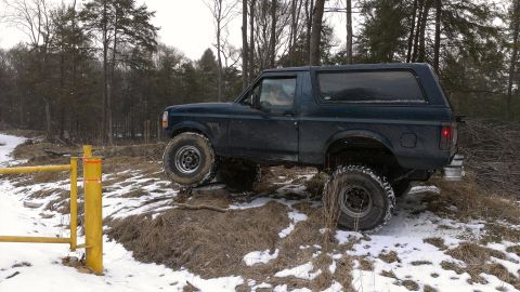 1995 Ford Bronco - A Ford Bronco navigates a snowy, off-road trail in a wooded environment.