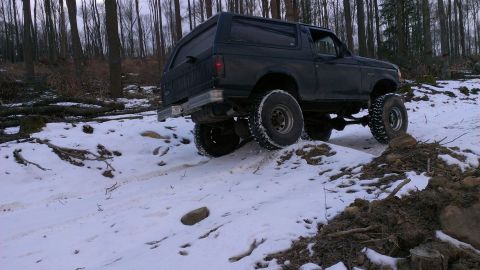 1995 Ford Bronco - A dark SUV navigates a challenging snowy terrain, its lifted suspension and large tires evident.