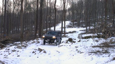1995 Ford Bronco - 1995 Ford Bronco navigating a snow-covered path through a dense forest.