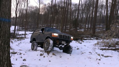 1995 Ford Bronco - A lifted Ford Bronco navigates a snowy, wooded path, its off-road capabilities.