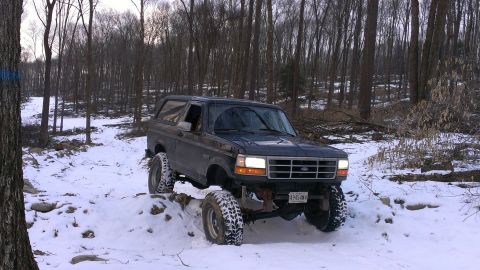 1995 Ford Bronco - A lifted Ford Bronco navigates a snowy, wooded path.