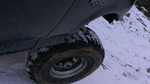 1995 Ford Bronco - A dark Ford Bronco navigates a snowy, off-road incline, with its tire and "BRONCO" badge clearly visible.