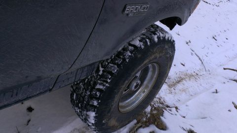 1995 Ford Bronco - A 1995 Ford Bronco XL is seen from the side, its tire covered in snow, navigating a snowy terrain.