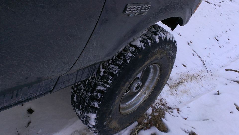 Dark 1995 Ford Bronco XL side view with knobby tire in snow