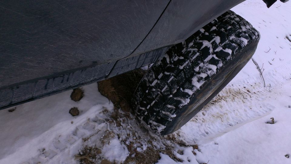 Close-up of a vehicle's tire partially buried in snow and mud