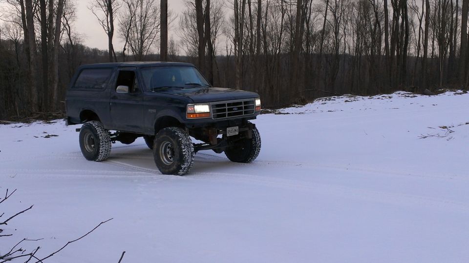 Dark SUV with lifted suspension driving in snow, front grille visible
