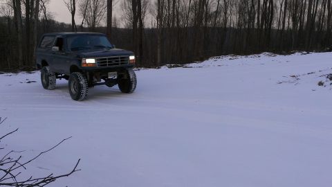 1995 Ford Bronco - A dark 1995 Ford Bronco with a lifted suspension navigates a snowy landscape.