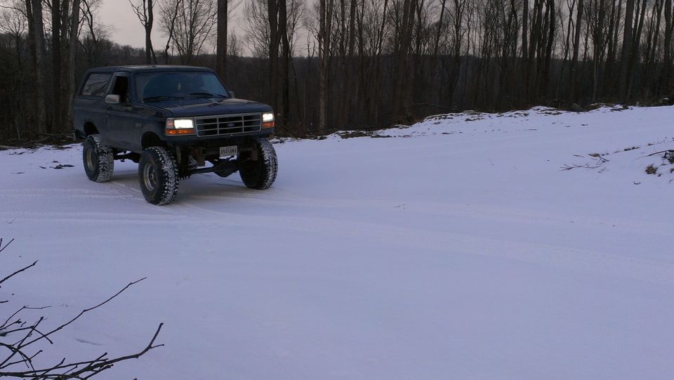 Dark 1995 Ford Bronco with lifted suspension driving in snow