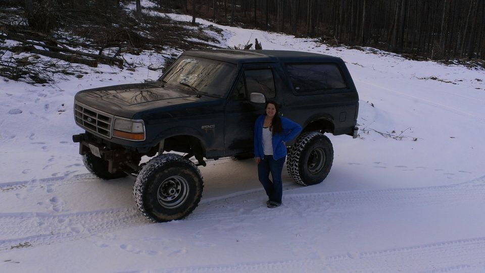 1995 Ford Bronco with lifted suspension and large tires parked in the snow with a person standing next to it