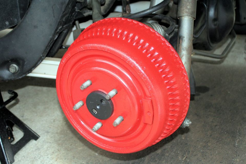 Red painted brake drum with five silver lug bolts and a black center cap, resting on a jack stand