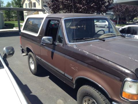 1992 Ford Bronco - A brown 1992 Ford Bronco with a white roof is parked in a lot, showing some wear and tear.