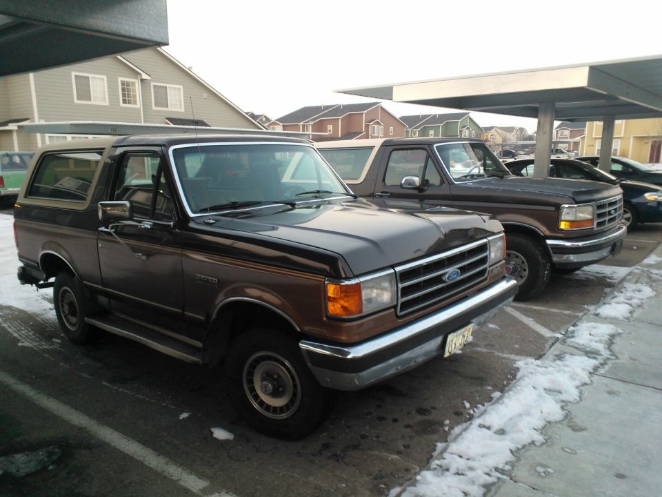 Brown Ford Bronco parked under a carport, with another truck behind it