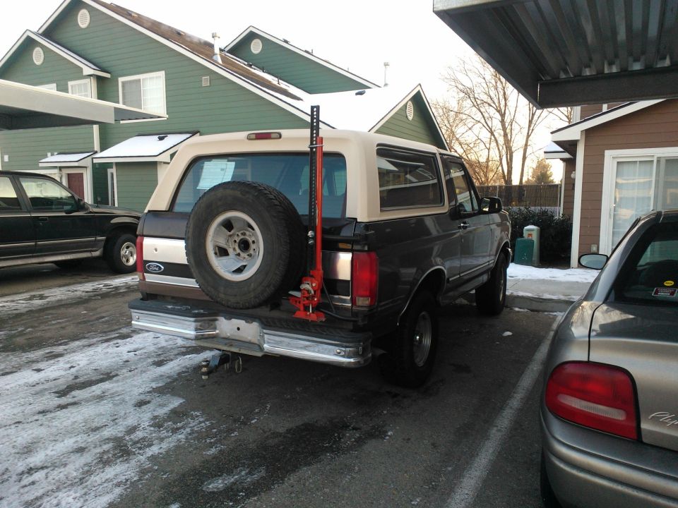 1992 Ford Bronco parked under a carport, spare tire mounted on rear, Hi-Lift jack attached