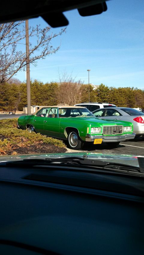 1971 Ford Ranchero - A green sedan with a white vinyl top is parked in a lot next to other vehicles.
