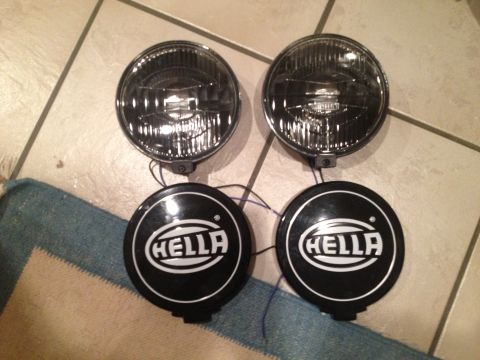 1996 Ford Bronco - A pair of Hella fog lights are displayed on a tiled floor, each with its protective cover.