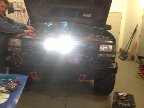 1996 Ford Bronco - A person works on the electrical system of a black SUV with its hood up and bright headlights illuminated.