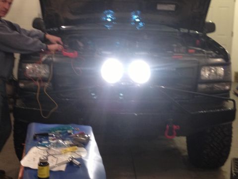 1996 Ford Bronco - A person is working on the electrical system of a truck with its hood open and auxiliary lights illuminated.