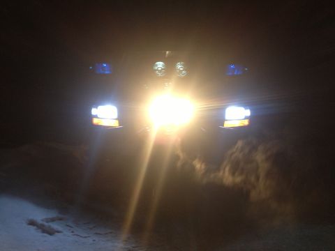 1996 Ford Bronco - Truck front with bright headlights on in the dark, snow on the ground.