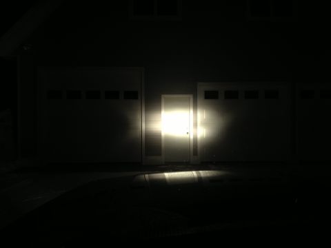1996 Ford Bronco - Bright headlights illuminate a central garage door at night.