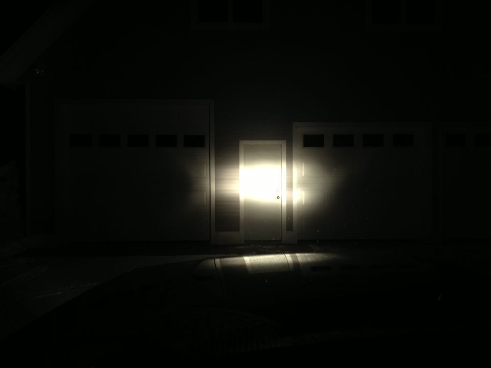 Headlights shine brightly on a white garage door between two other garage doors
