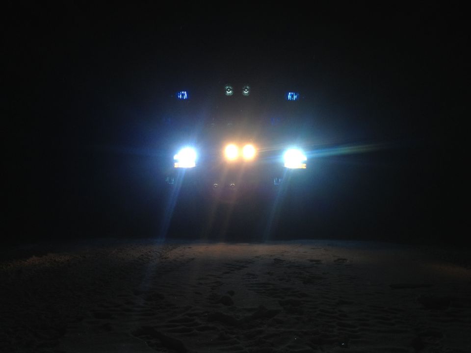 Front view of a dark-colored 1992 Ford Bronco with headlights and auxiliary lights illuminated at night