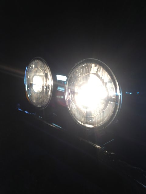 1996 Ford Bronco - Close-up view of two illuminated headlights on a dark vehicle.