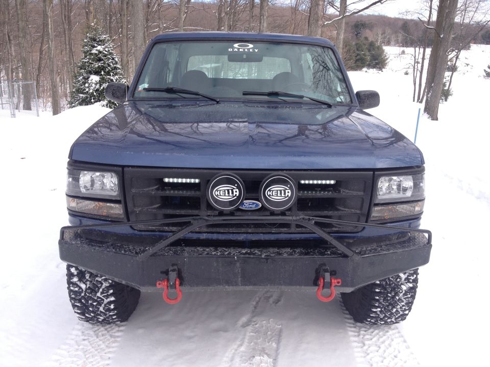Front view of a blue 1996 Ford Bronco with a custom bumper and Hella lights in the snow