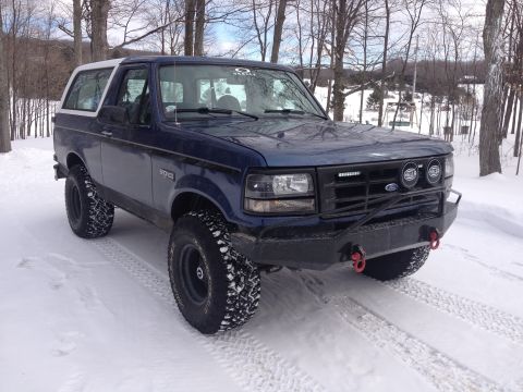 1996 Ford Bronco - A blue 1996 Ford Bronco with a white roof and aftermarket bumper is parked in the snow.