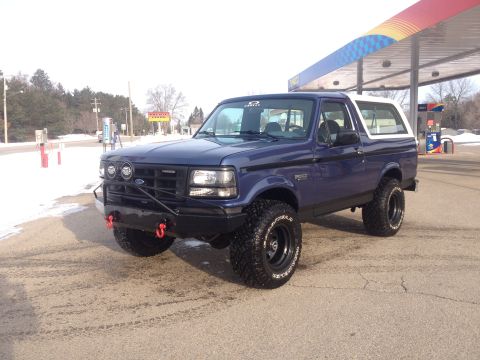 1996 Ford Bronco - A blue 1996 Ford Bronco is parked at a gas station with a white removable top and off-road tires.