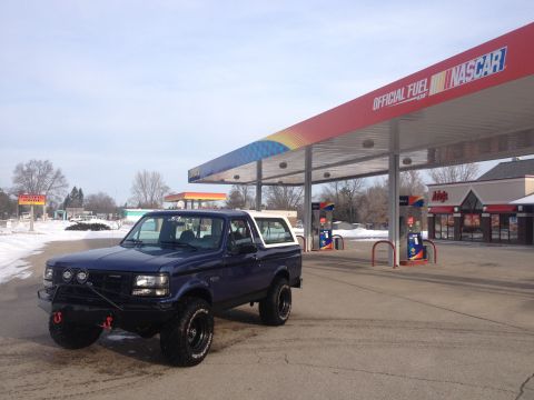 1996 Ford Bronco - A blue SUV with a white top is parked at a gas station under a red awning with NASCAR branding.