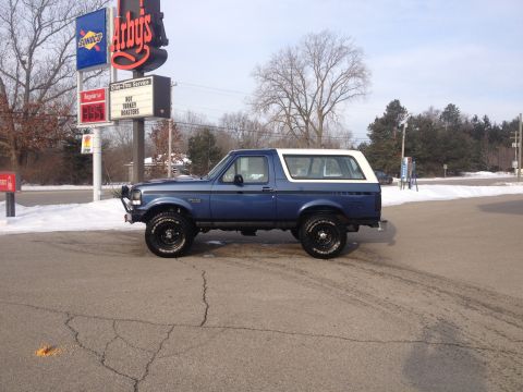 1996 Ford Bronco - Side view of a blue Ford Bronco with a white top, parked in a lot with snow on the ground.