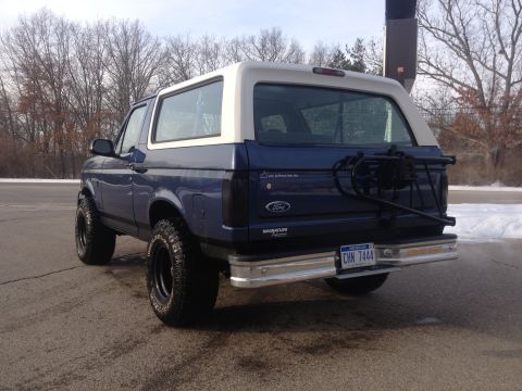1996 Ford Bronco - Rear view of a blue and white Ford Bronco with a spare tire carrier and custom wheels.