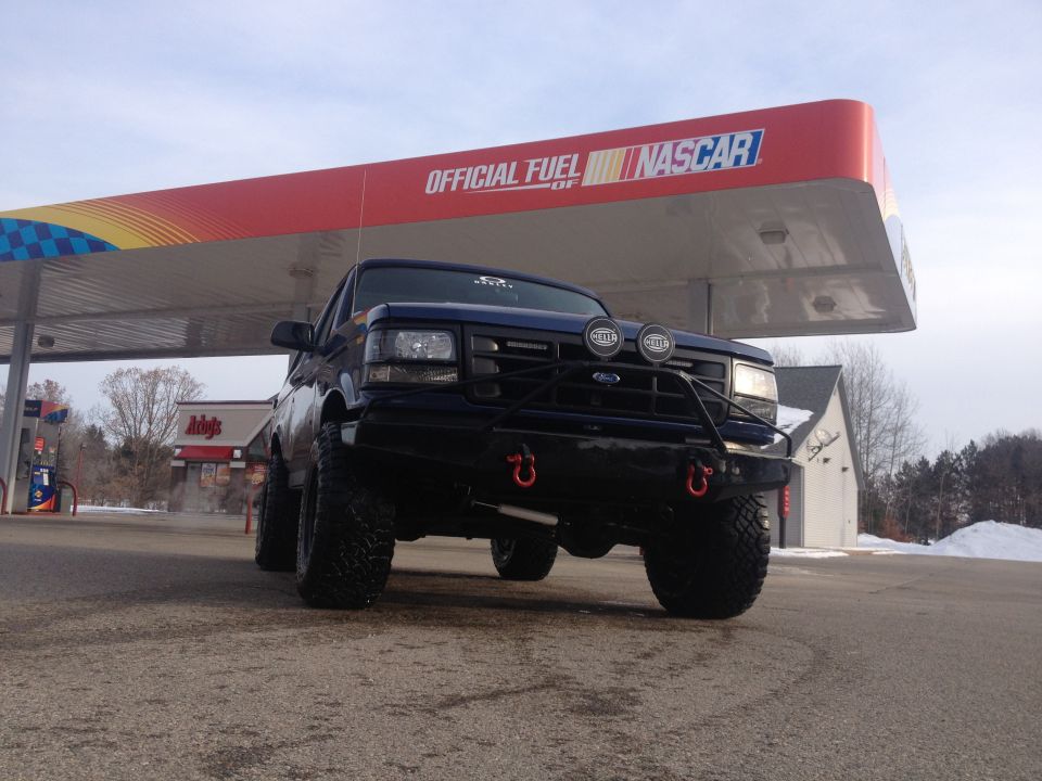 Dark blue 1996 Ford Bronco with aftermarket bumper and lights at a gas station