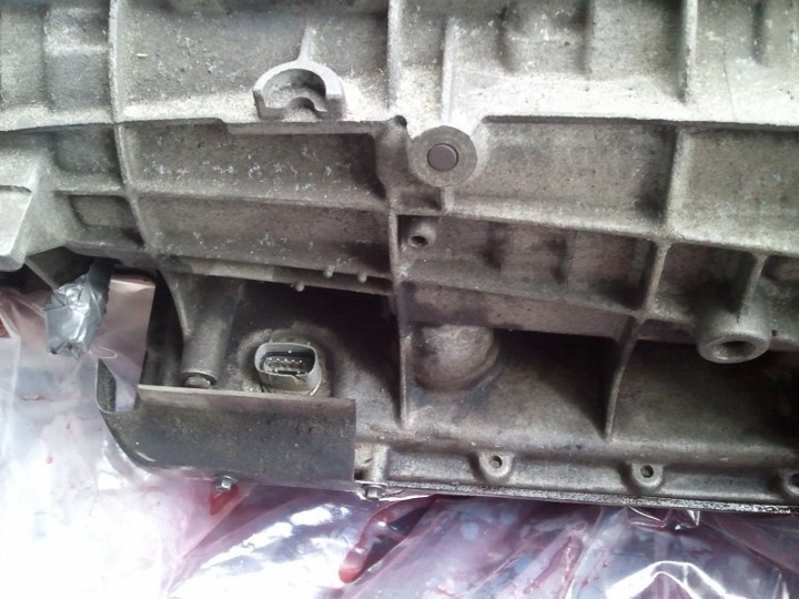 Close-up of a dirty, gray metal transmission housing with a wiring connector visible