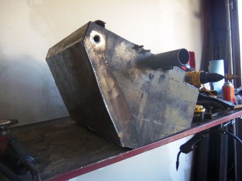 1968 Ford Bronco - A fabricated metal tank with a pipe fitting sits on a shelf in a workshop, next to tools and supplies.