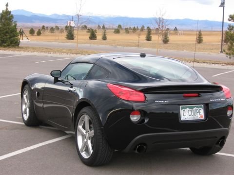 1995 Ford Bronco - Black Pontiac Solstice GXP Coupe parked in a lot with mountains in the background.