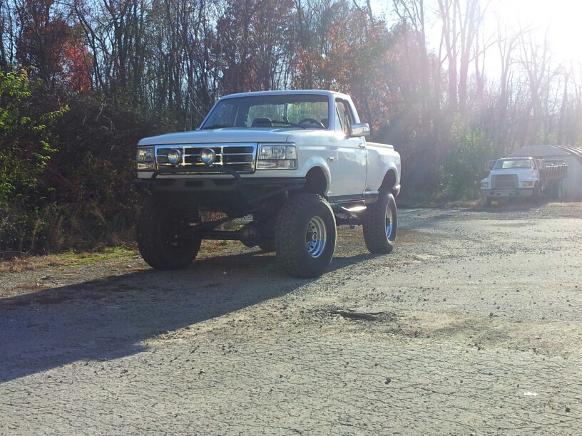 White 1995 Ford F-150 with large tires and lift kit, front 3/4 view