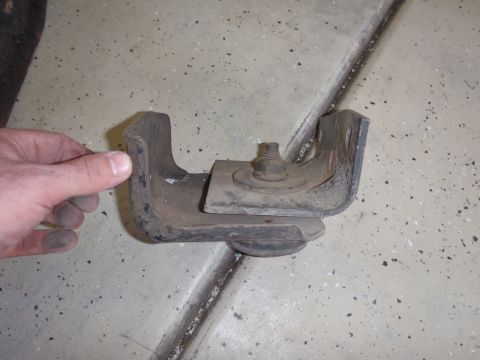 1978 Ford Bronco - A metal bracket with a rubber isolator and bolt is shown, held by a hand over a concrete floor.