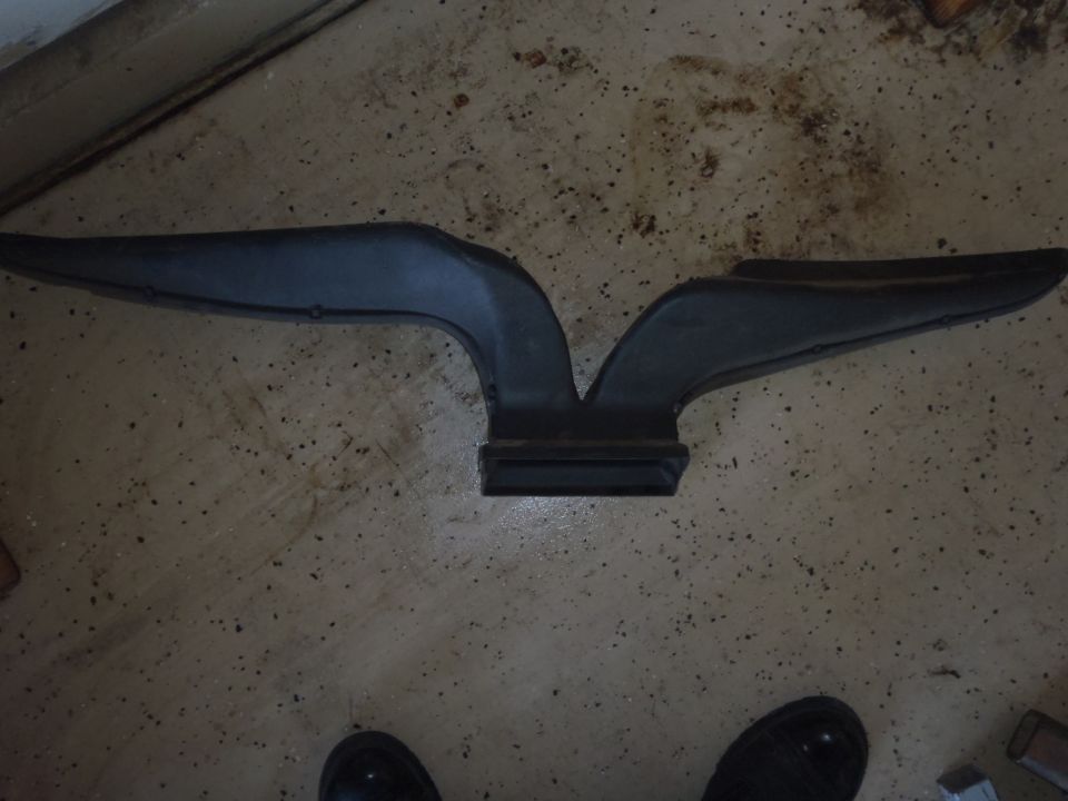 Black plastic air intake duct with a V-shaped design, lying on a speckled concrete floor