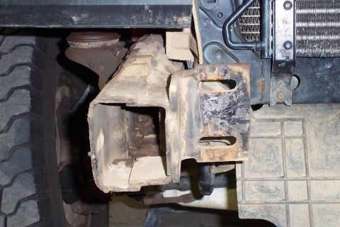1996 Ford Bronco - Close-up underside view of a vehicle's front frame section showing a rusty, dirt-caked frame rail and mounting bracket, with a tire visible…